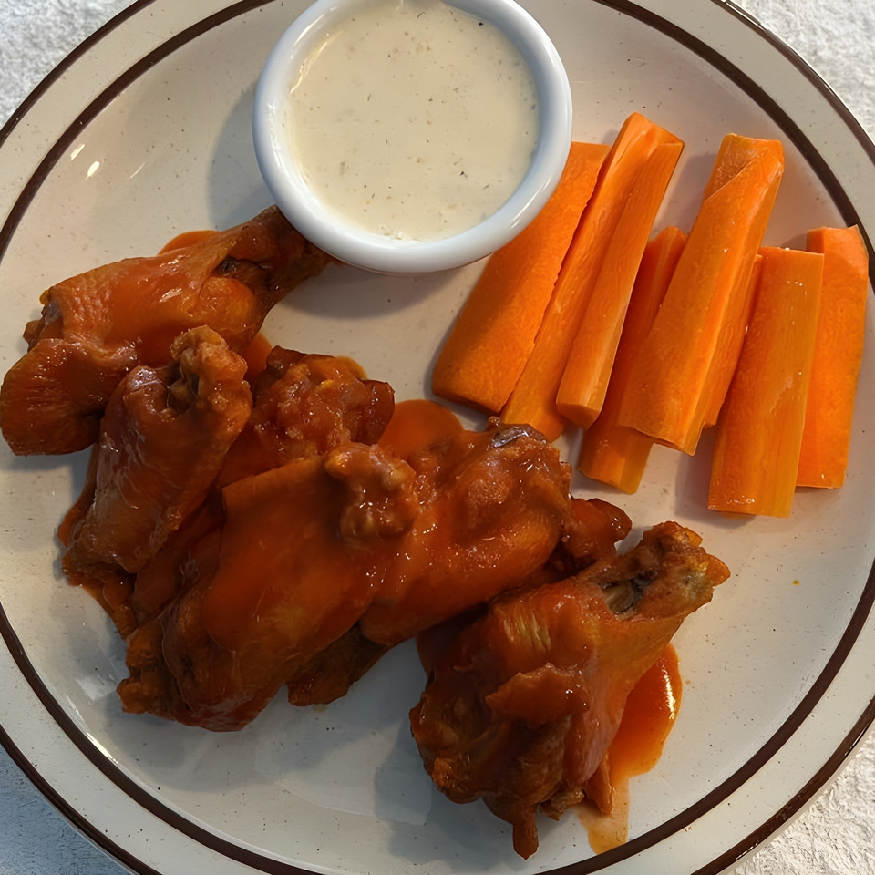 Plate of buffalo wings with ranch dipping sauce and carrot sticks.