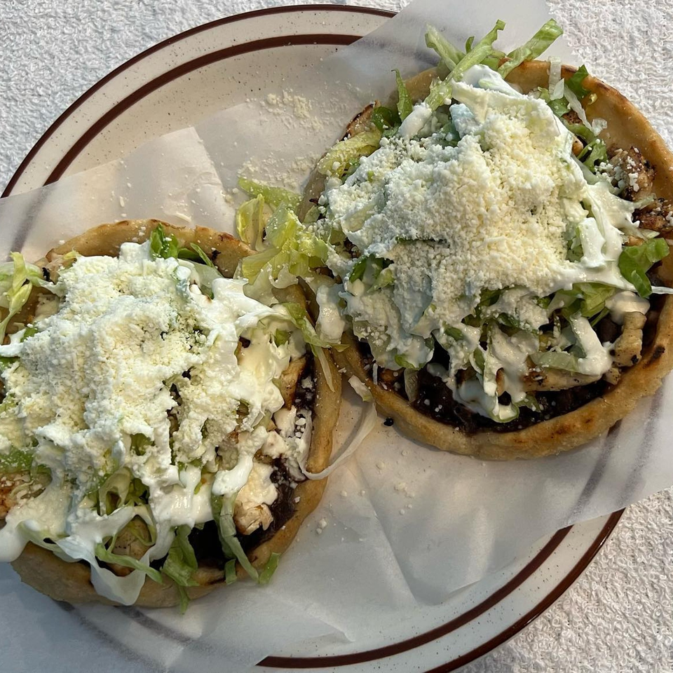 Two La Fortuna sopes topped with lettuce, crema, and crumbled cheese on a plate.